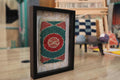 moroccan rug, circular wool rug art, hand-knotted framed tapestry, green red spiral rug, framed moroccan textile, miniature rug wall hanging, artisan moroccan decor, target motif rug, knot by knot rug weaving
