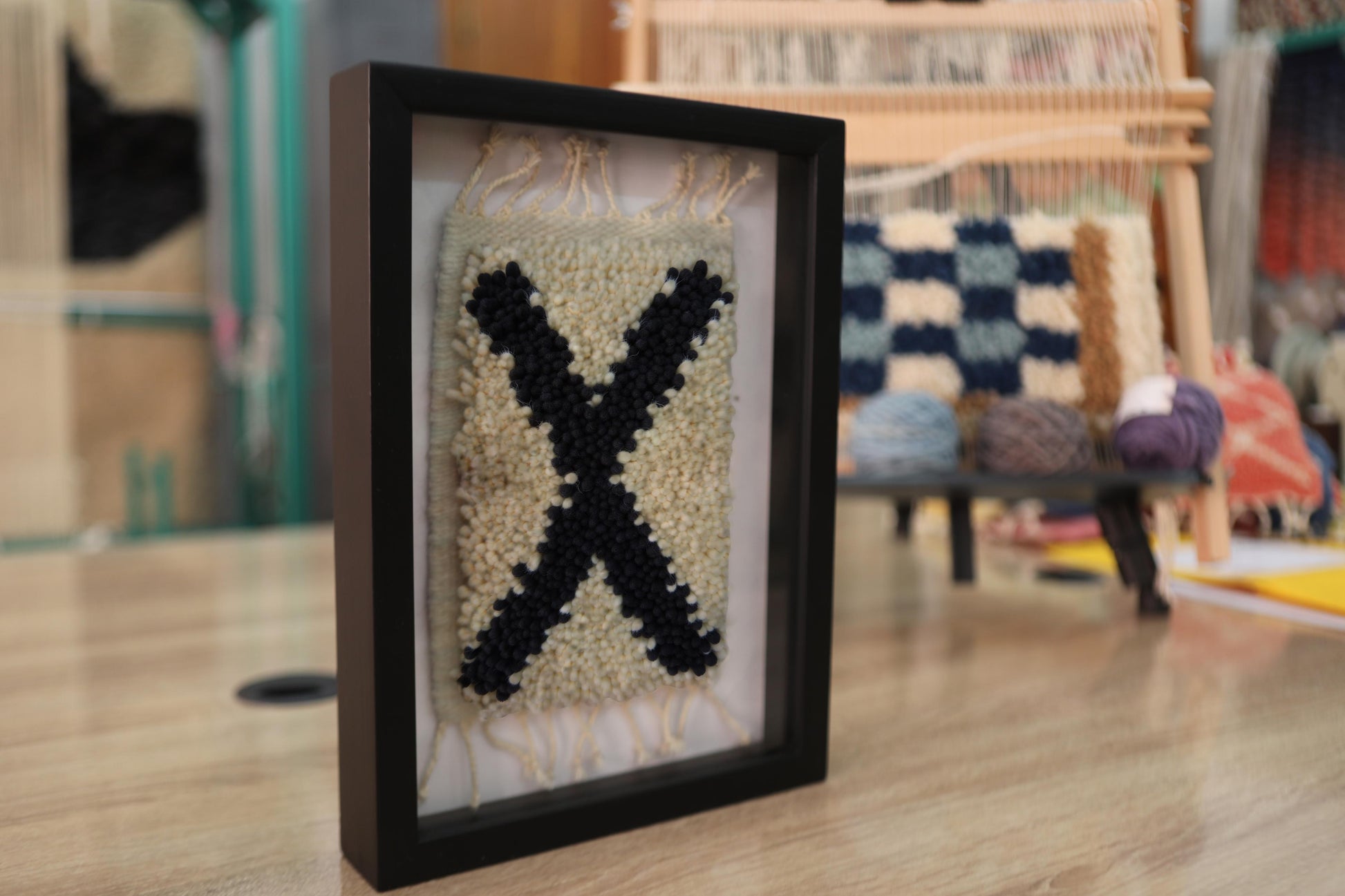 moroccan rug wall art, black x rug, framed wool wall hanging, boho wall decor, handmade moroccan textile, hand-knotted wall art, knot by knot weaving, tribal rug decor, small framed rug, artisan moroccan wall art
